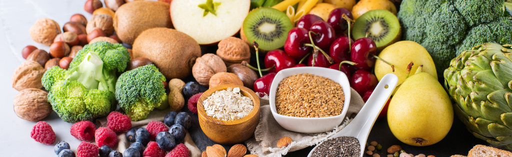 Various fresh foods – vegetables, fruit, nuts, seeds and grains – arranged in bowls and scattered across a surface