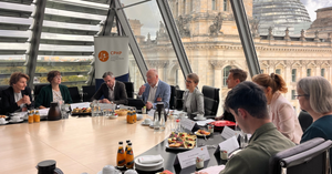 Menschen sitzen an einem großen Tisch in einem Raum mit Glasfassade und Blick auf das Reichstagsgebäude.