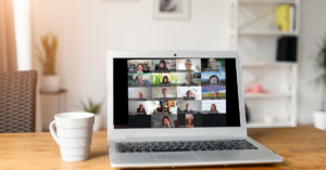 Laptop auf einem Holztisch mit einer Videokonferenz, auf dem Bildschirm sind mehrere Personen in kleinen Fenstern zu sehen